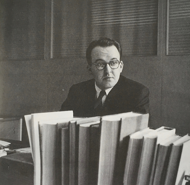 Robert Fulford in suit and tie, with books